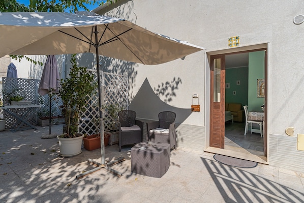An outdoor patio with a table and chairs, a potted plant, and a large umbrella.