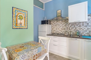 A kitchen with a tiled backsplash, a stove, a microwave, and a table with a patterned tablecloth.