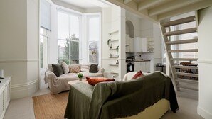 A spacious living room with a sofa, coffee table, and a staircase leading to an upper floor. - GuestReady - Cosy Loft Studio in Chiswick (London)