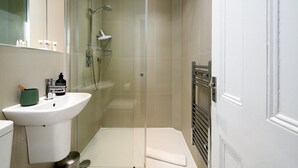 A modern bathroom with a glass shower enclosure, a white sink, and a towel rack. - GuestReady - Cosy Loft Studio in Chiswick (London)