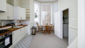 A kitchen with white cabinets, a wooden countertop, a sink, and a stove. There is a dining area with wooden chairs and a table. - GuestReady - Cosy Loft Studio in Chiswick (London)