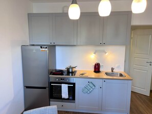 A compact kitchen with a refrigerator, oven, and a kettle on the countertop.