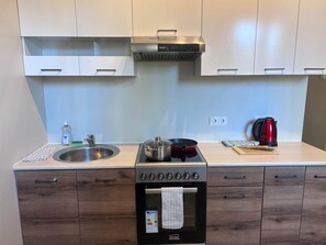 A compact kitchen with a stainless steel sink, a red electric stove, a built-in oven, and wooden cabinets. - 2-Bedroom apartment in the City center (Tallinn)