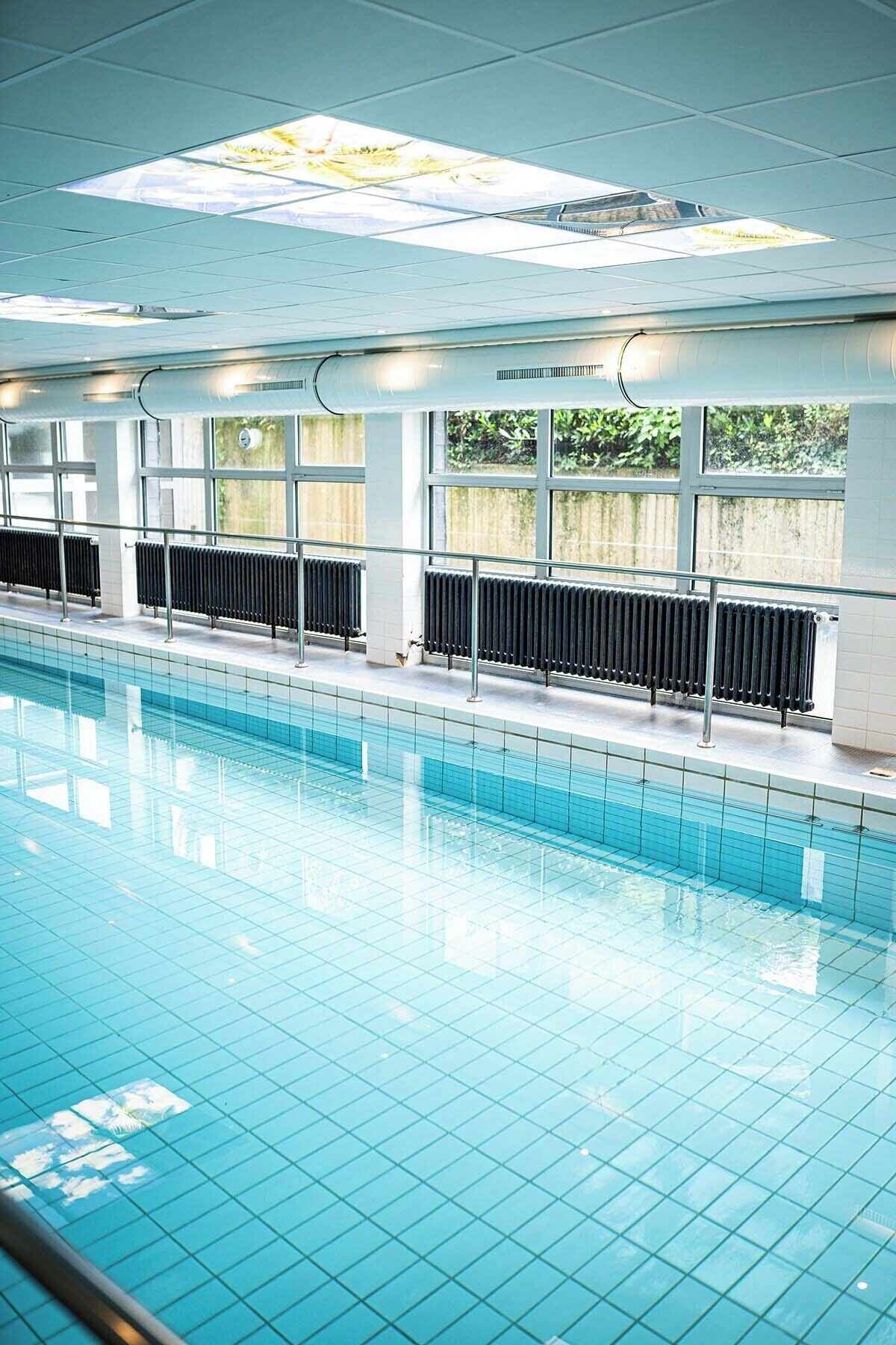 A swimming pool with clear blue water, surrounded by windows and a tiled floor.