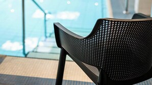 A modern indoor pool area with a clear view of the pool, a black chair in the foreground, and a glass railing along the pool's edge. - Hotel floor C (Winterberg)