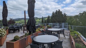 An outdoor patio with round tables and chairs, covered by umbrellas, overlooking a scenic landscape. - Hotel floor C (Winterberg)