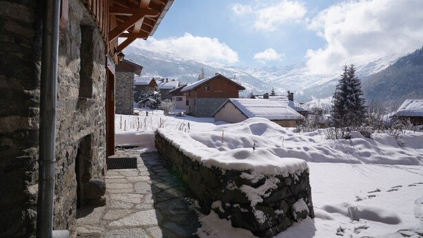 Ein Steinhaus mit Holzdach, verschneitem Untergrund und einer Bergkulisse.
