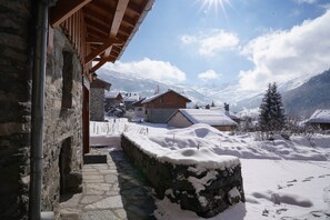 A stone building with a wooden roof, snow-covered ground, and a mountainous backdrop.