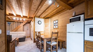 Ein Holzinterieur mit Esstisch, Stühlen, einem Kühlschrank und einer Wanduhr.