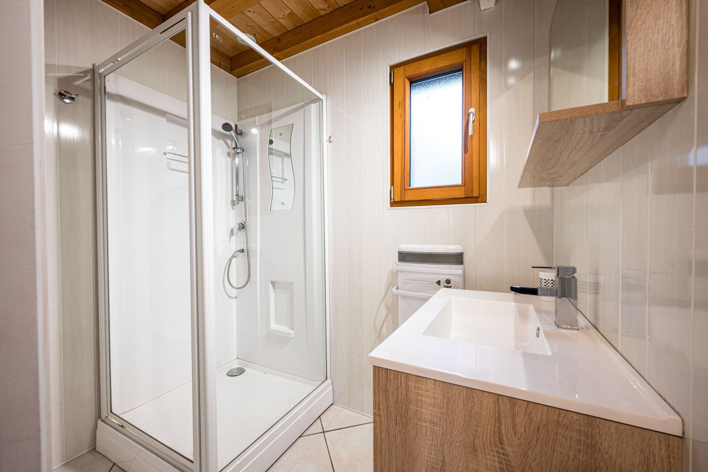 A modern bathroom with a glass shower enclosure, a white sink, and a wooden vanity.