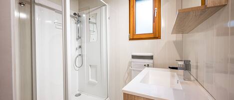 A modern bathroom with a glass shower enclosure, a white sink, and a wooden vanity.