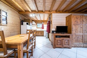 A wooden interior with a dining table, chairs, a television, and cabinets.
