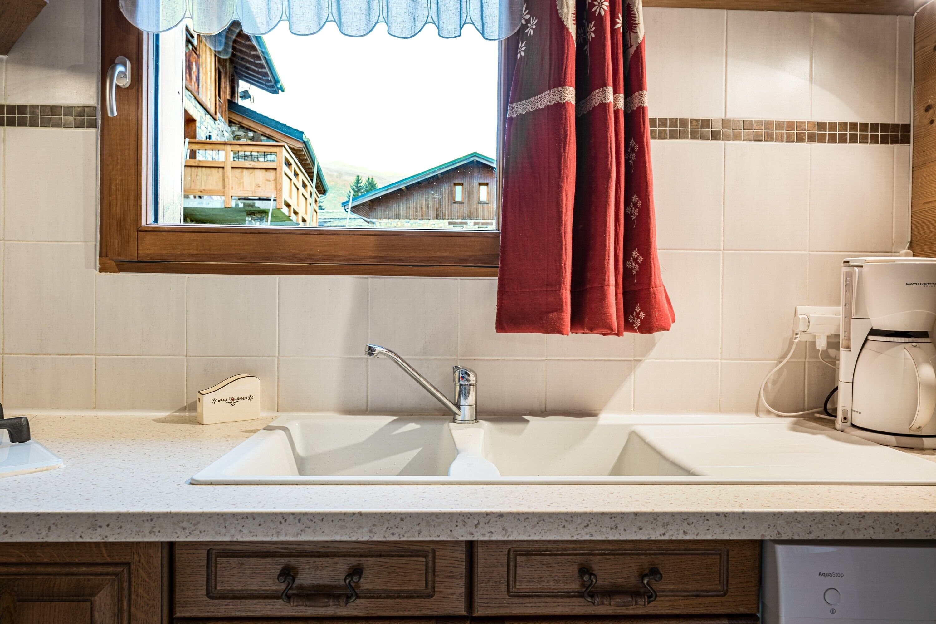 A kitchen with a sink, a coffee maker, and a window with a view of buildings.
