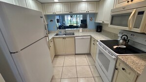 A compact kitchen with white cabinets, a dishwasher, a stove, and a microwave.