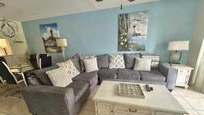 A living room with a grey sectional sofa, a white coffee table, and a painting of a bird on the wall.