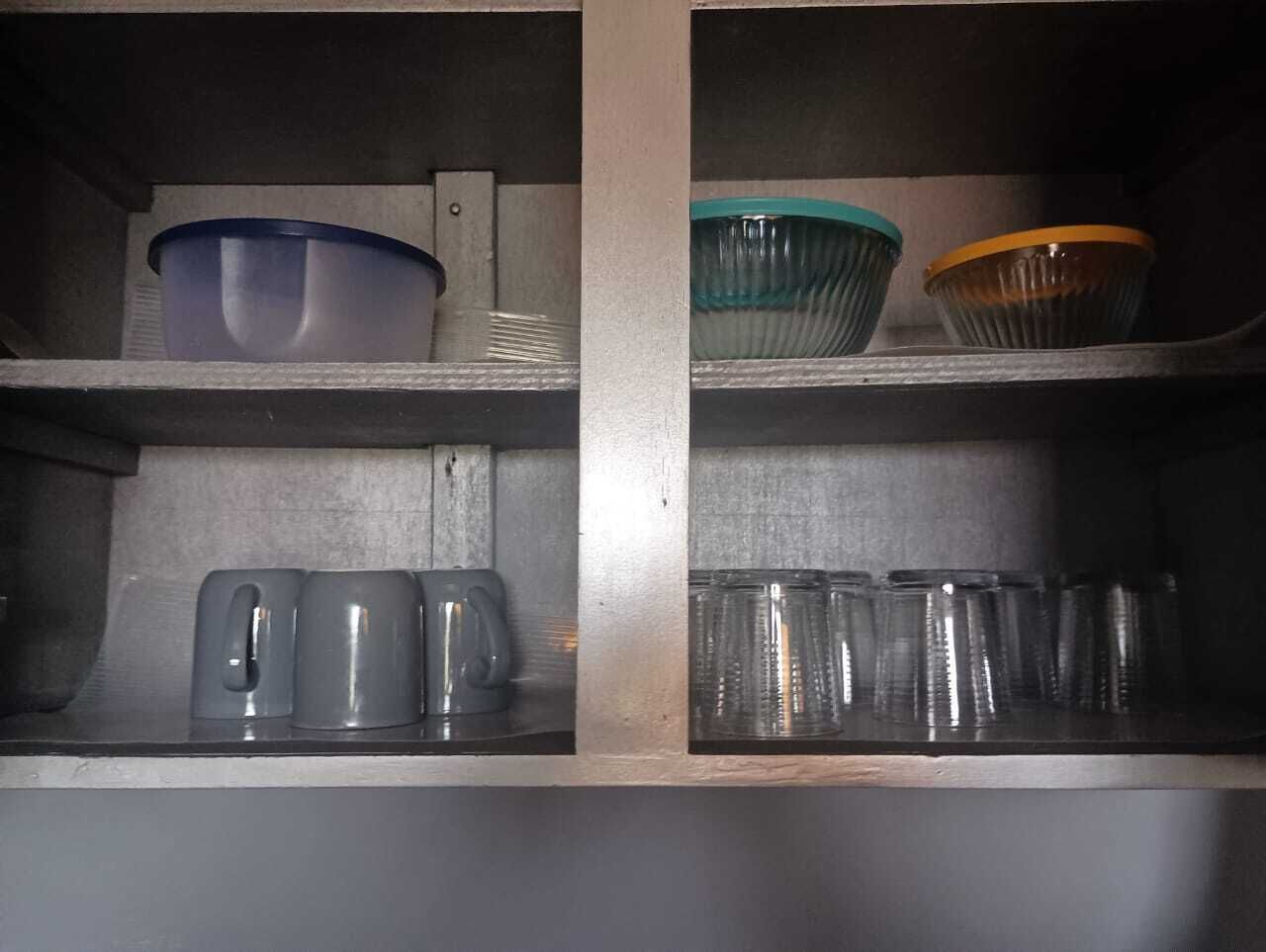 A kitchen with two shelves; the top shelf has a blue bowl and a green bowl, and the bottom shelf has two kettles and several glass cups.