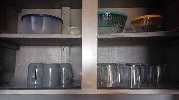 A kitchen with two shelves; the top shelf has a blue bowl and a green bowl, and the bottom shelf has two kettles and several glass cups.