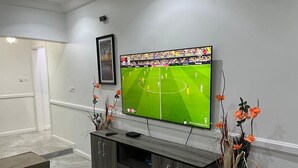 Un saló amb un televisor de pantalla plana fixat a la paret, un moble de divinització de fusta fosca i un ram de flors taronges.