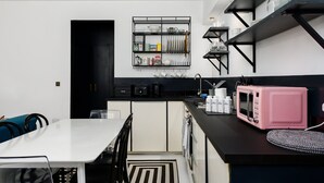 A modern kitchen with black and white cabinetry, a white dining table, and a pink microwave.