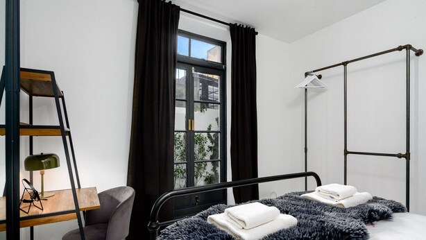 A modern bedroom with a bed, a desk, a chair, and a window with curtains.