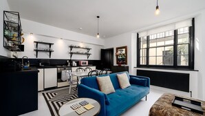 A modern kitchen with white cabinets, a black countertop, and a dining area with a blue sofa and a small round table.