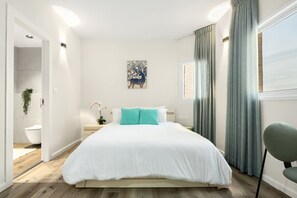 Ein modernes Schlafzimmer mit einem großen Bett, einem Nachttisch, einer Wandlampe und einem Fenster mit Vorhängen.