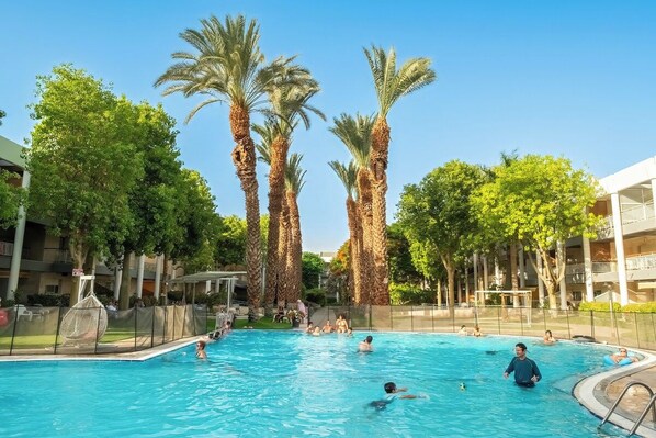 Una piscina rodeada de palmeras y un edificio con balcones.