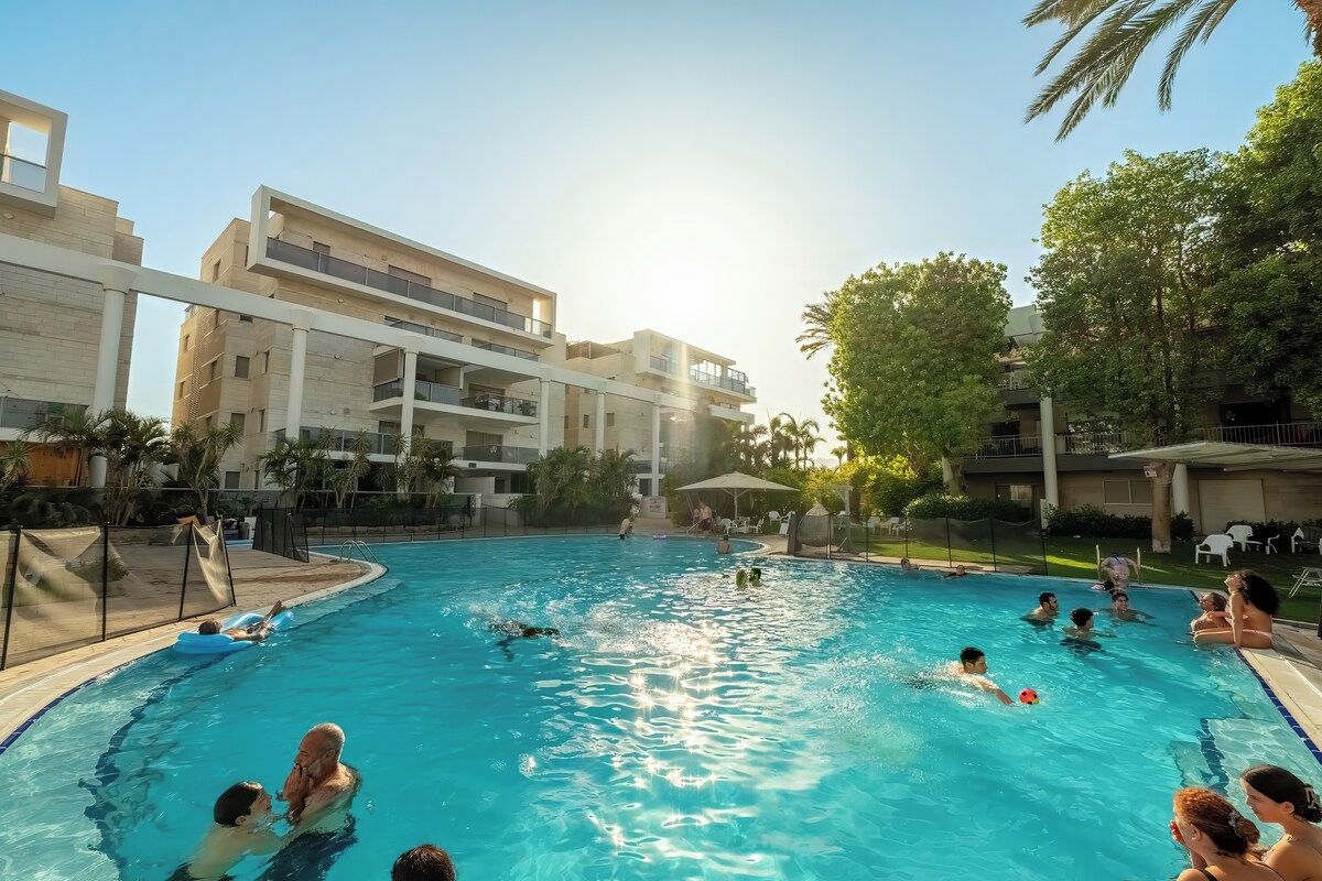 Una piscina rodeada de edificios, con gente nadando y descansando.