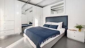 A modern bedroom with a large bed, built-in wardrobe, and a bedside table with a plant.
