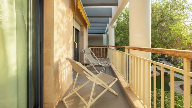 A balcony with a white railing, a pair of white lounge chairs, and a small table.