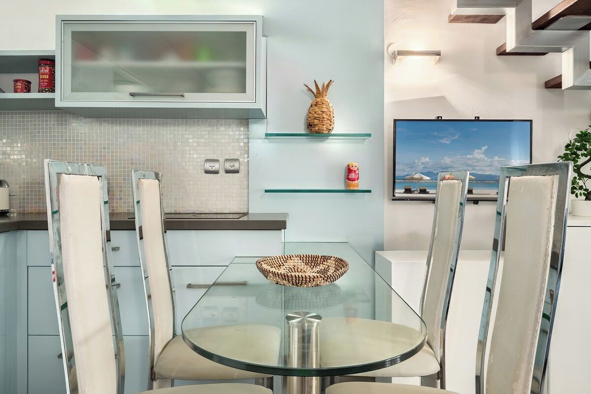 Una cocina moderna con una mesa de vidrio, sillas y un televisor.