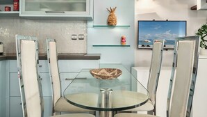 A modern kitchen with a glass dining table, chairs, and a television.