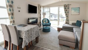 Ein Wohnzimmer mit Fernseher, einer Couch, einem Esstisch mit Stühlen und Blick ins Freie.