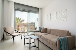 Una sala de estar moderna con sofá, sillón y mesitas, un balcón con vistas, y obras de arte en la pared.