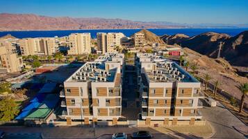 Un immeuble d’appartements moderne doté d’une cour intérieure, entouré de collines désertiques et offrant une vue sur la mer.