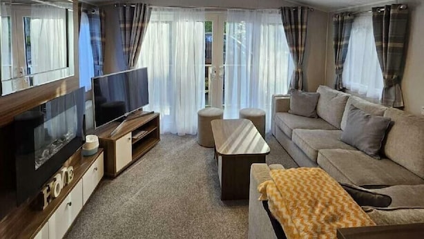 A modern living room with a flat-screen TV, sofa, ottoman, and a coffee table. - 145 Woodside View (Caernarfon)