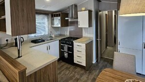 A modern kitchen with a central island, wooden cabinets, and a built-in stove. - 145 Woodside View (Caernarfon)