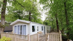 A mobile home with a deck, surrounded by trees. - 145 Woodside View (Caernarfon)