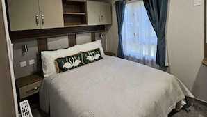 A bedroom with a bed, a nightstand, a wardrobe, and a window with curtains. - 145 Woodside View (Caernarfon)