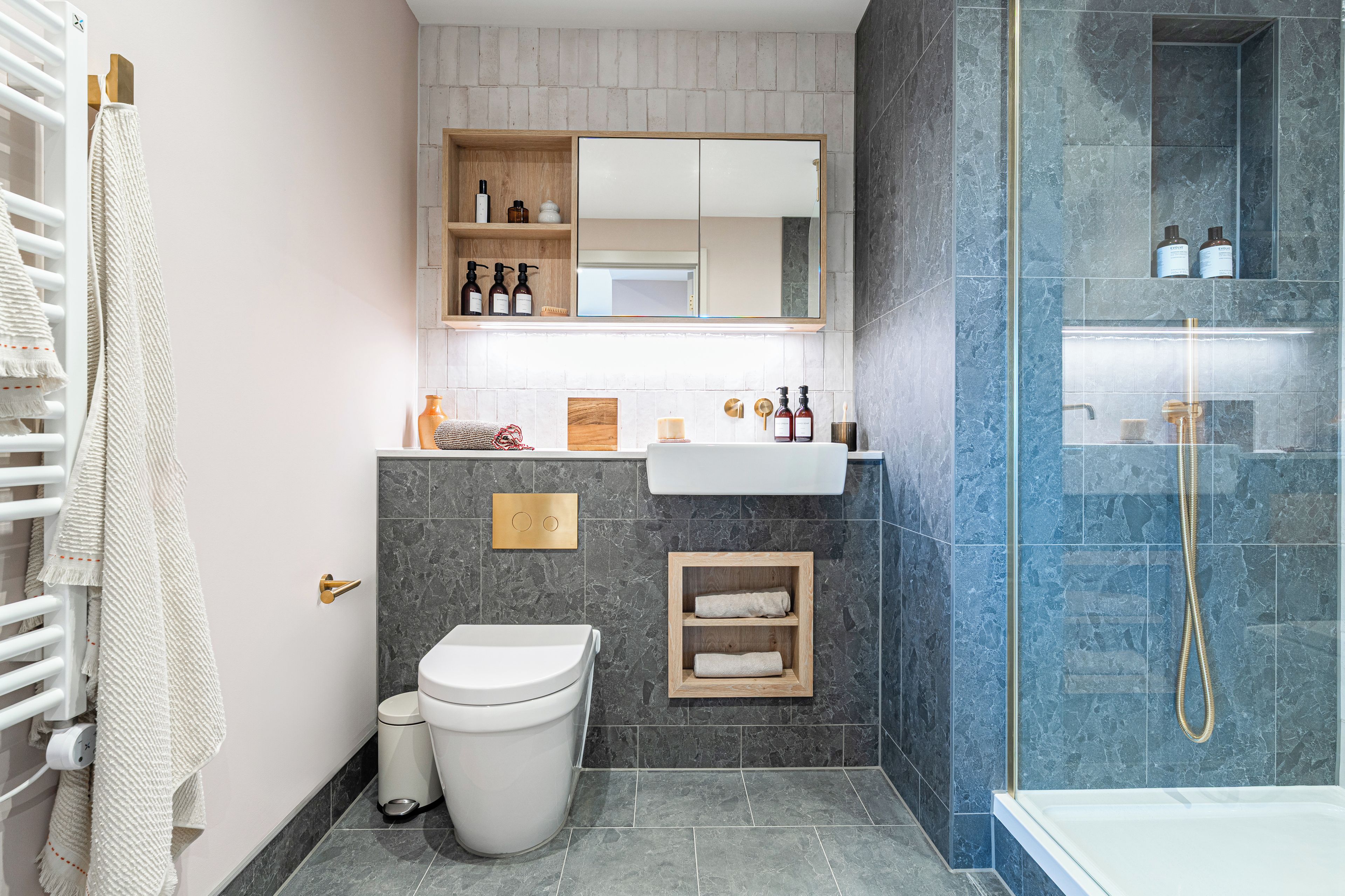 A modern bathroom with a toilet, sink, and shower. There are shelves with toiletries and a mirror above the sink.