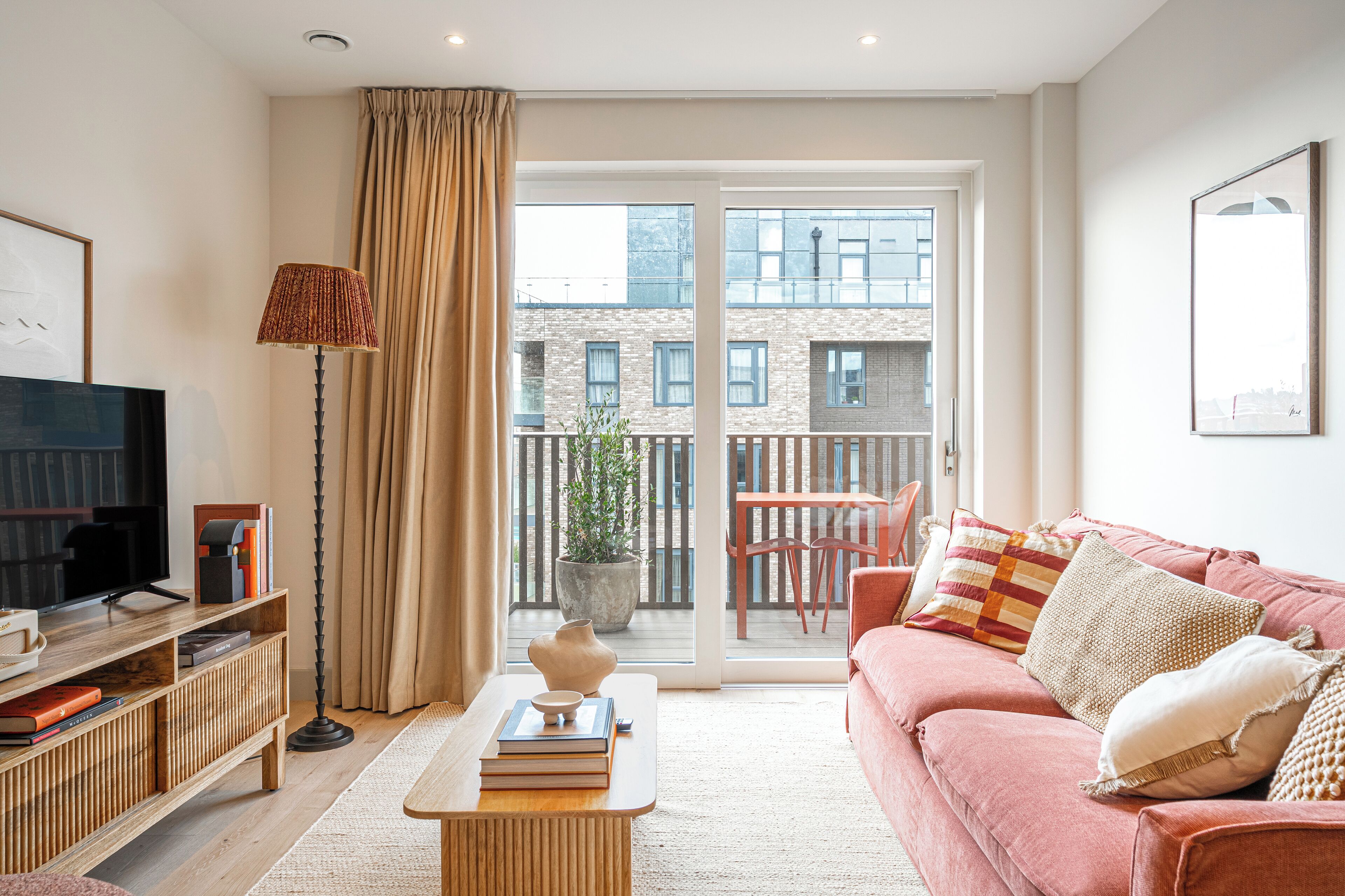 A modern living room with a sofa, a coffee table, a TV, and a balcony with a view of buildings.