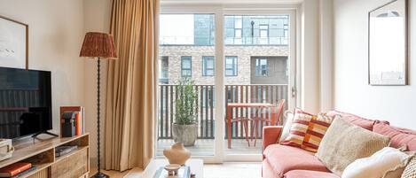 A modern living room with a sofa, a coffee table, a TV, and a balcony with a view of buildings.
