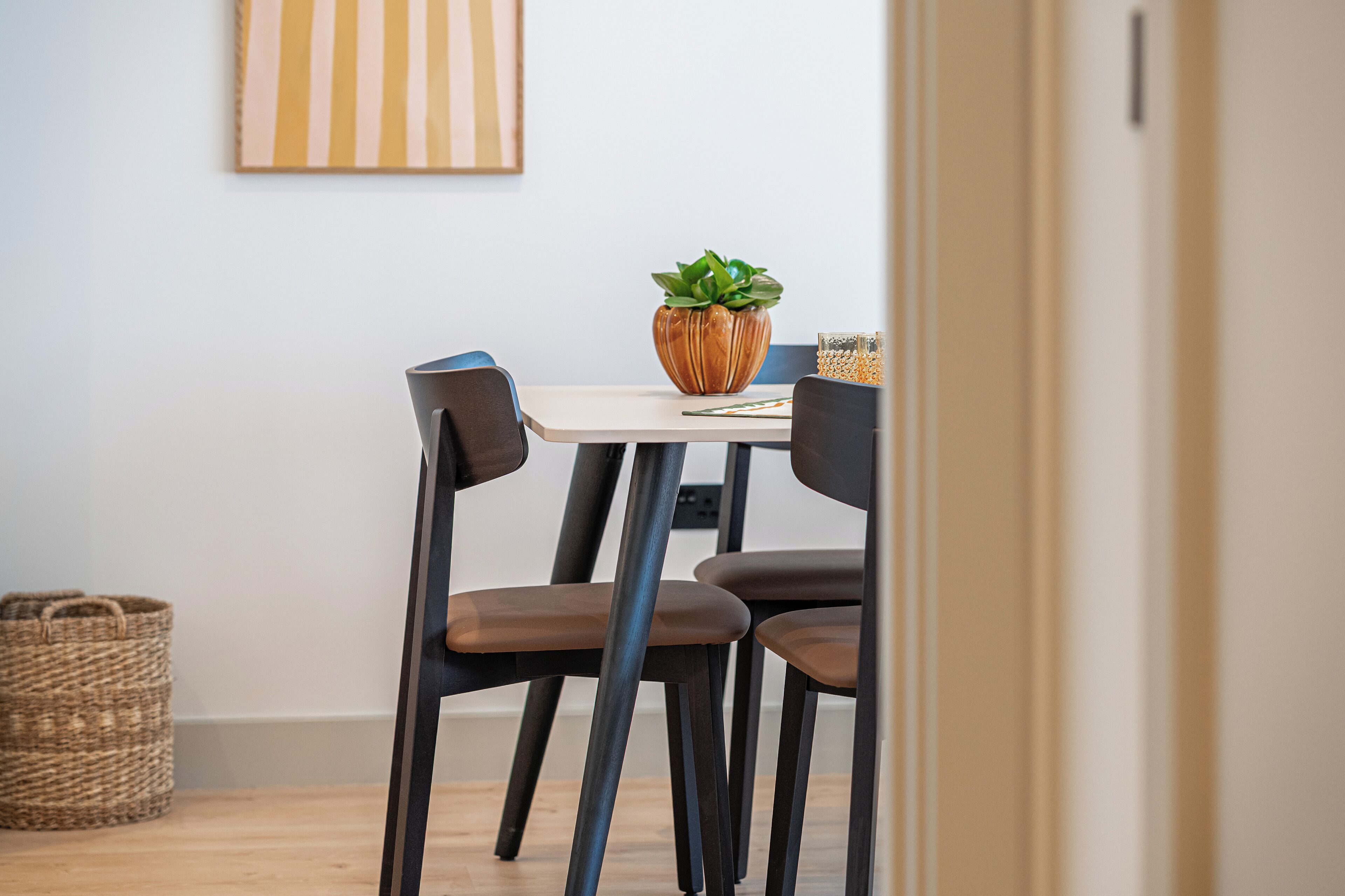 Un espace repas comprenant une table, des chaises, une plante en pot et un tableau accroché au mur.