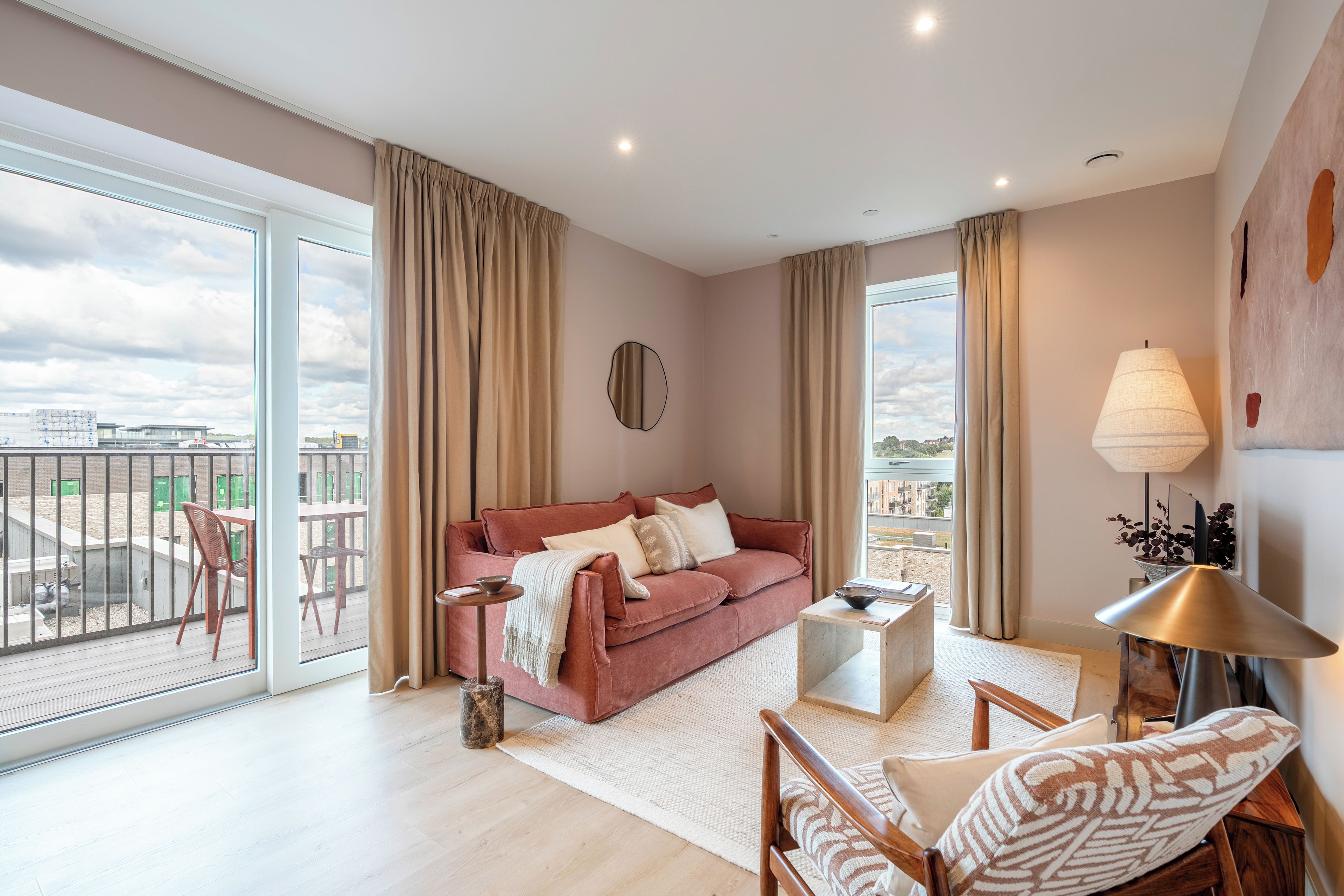 A spacious living room with a large window, a red sofa, a coffee table, and a balcony with outdoor furniture.