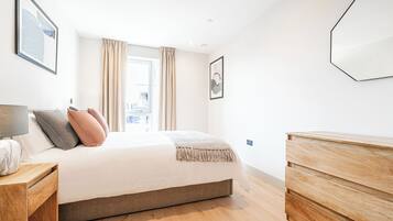 Un dormitorio moderno con una cama grande, un aparador de madera y vistas a la ciudad a través de la ventana.