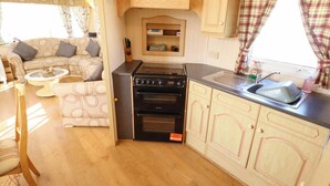 Una cocina compacta con estufa, horno y lavabo, contigua a una sala de estar con sofá y mesa de centro.