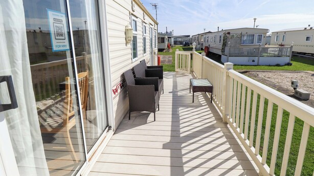 Una terraza cubierta al aire libre con mobiliario exterior, una cerca blanca y vistas a otras casas móviles.