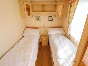 Ein Schlafzimmer mit zwei Einzelbetten, Holz-Kopfteilen, einem kleinen Nachttisch und einem Regal über den Betten.