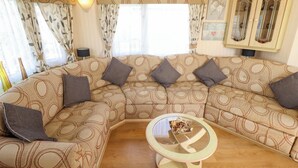 Una sala de estar con un sofá seccional, una mesa de centro de vidrio y un mueble con puertas de cristal.