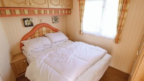 Un dormitorio con cama, cabecera de madera, mesita de noche y ventana con cortinas.